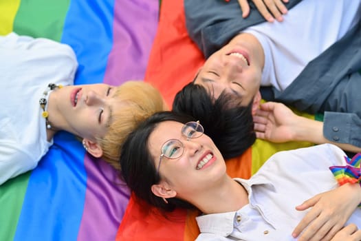 Above view shot of happy young LGBT friends lying on rainbow flag, supporting LGBTQ community and equality social.