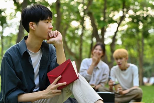 Pensive asian student man sitting outside of university building and looking thoughtfully. Youth lifestyle and education concept.