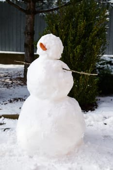 Still life with a white snowman in the snow covered backyard over evergreen spruce background. Christmas time. The concept of wonderful wintertime, winter holidays and outdoors winter leisure games