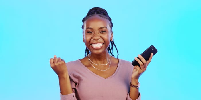 Wow, happy and excited black woman with phone receiving email news of bonus, promotion or announcement in studio. Winning, prize notification and African girl celebrating with smile on blue backgrou.