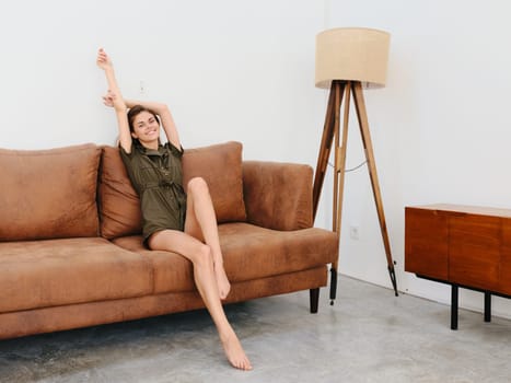 Young woman model sitting on the couch at home smiling and relaxing, modern interior lifestyle. High quality photo