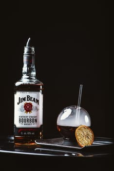 Jim Beam is one of best selling brands of bourbon. Alcohol with smoke. Jim Beam bottle arranged with a spherical glasses on black background. Odessa, Ukraine - February 07, 2020