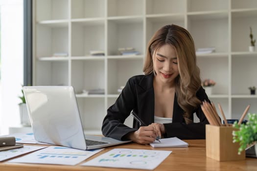 Business woman hand working at a computer and writing on a notepad. business financial concept.