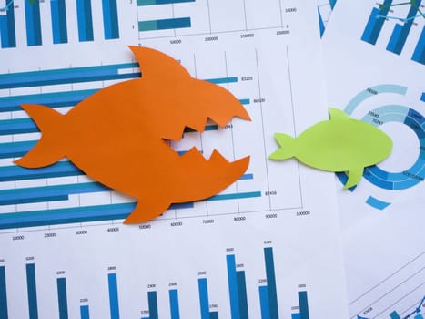 Mergers and acquisitions concept. Two paper fish on financial charts.