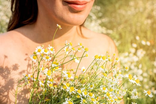 Woman holds daisies in her hands in the field in summer day