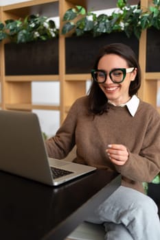 Woman Wearing Glasses using Laptop. Smiling businesswoman in eyeglasses and casual clothes working with laptop computer watching screen. Elegant business female medium vertical shoot