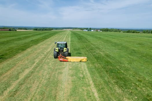 Tractor effectively cuts the grass using its rotary mower. Mowing grass in farmer's field.
