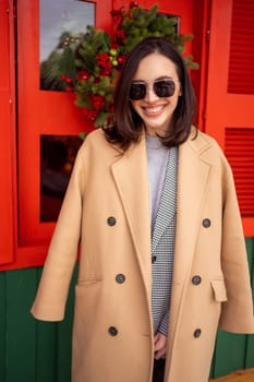 Happy caucasian girl walking sunny winter Christmas holiday in European city. Brunette woman wears stylish jacket, coat and sunglasses. Positive emotions lifestyle concept