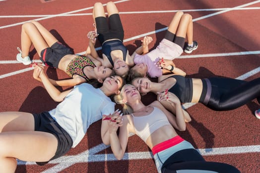 Group of tired and happy fit young girls resting on floor at stadium