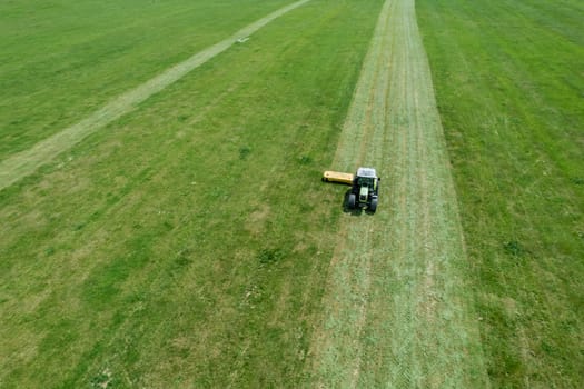 Top view of mowing grass on field. Grass is being efficiently trimmed by tractor's rotary cutting implement.