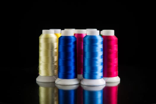 set of different color sewing threads, isolated on black background.