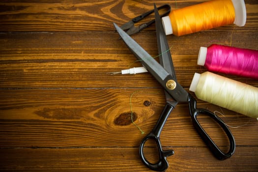 a set of tools and threads for sewing clothes, on a wooden background.