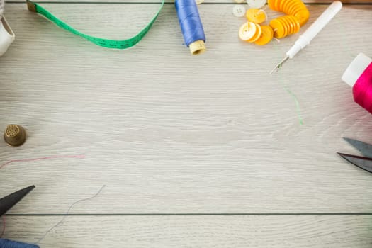 a set of tools and threads for sewing clothes, on a wooden background.