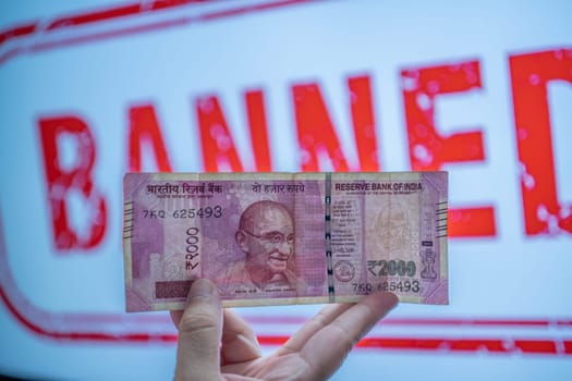 holding a Rs 2000 Indian bank note that has been removed from circulation through demonitization to reduce black money in front of banner saying banned in India