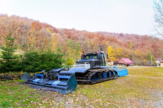 Crawler tractor is standing near the forest in the autumn season. Snow removal equipment snow in mountainous terrain.