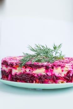 Russian salad - herring under a fur coat, herring salad with potatoes, eggs, beets, carrots, and mayonnaise on a white square plate