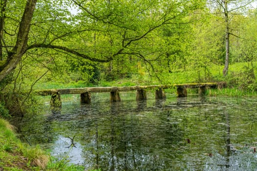Old stone slab granite bridge across a pond or calm lake in English park land