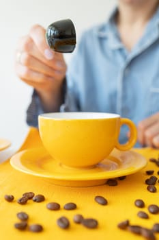 A young woman prepares herself coffee in a bright yellow mug. Grains of coffee on the table. Enjoy fresh aromatic coffee