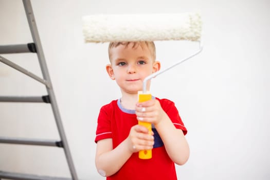 Little boy standing with paint roller near white wall. Redecoration, repair and repaint concept