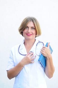 Young beautiful caucasian woman doctor with a phonendoscope on her neck and with a notepad smiling on a light background. High quality photo