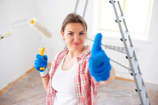 Beautiful woman with roller painter showing thumb-up while doing repair in room.