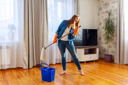 Funny happy young woman with mop singing, dancing and having fun while cleaning floor. Housewife enjoying domestic chores, doing home cleanup creatively