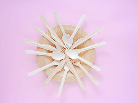Plate and kitchenware utensils on pink paper background Wooden biodegradable dishes. Eco-friendly choice and nature friendly. The concept of a world without plastic and a clean planet. Space for text