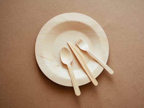 Ecology, zero waste. Top view of wooden, biodegradable, eco friendly tableware set on the plate on craft paper background. Concept of environment preservation and protection. Cope space, flat lay