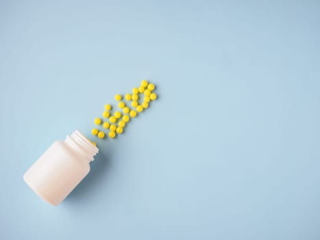 Pharmaceutical and health care concept. Minimalism style template for medical blog. White medicine bottle and small round yellow pills spilled out blue paper background. Medicine pills. Flat lay