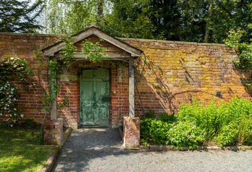 Painted green door and wooden porch as entrance to walled garden made with brick