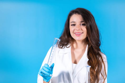 Brown-haired laboratory assistant holds couple of transparent test tubes for liquids. Woman enjoys working in laboratory at blue wall studio