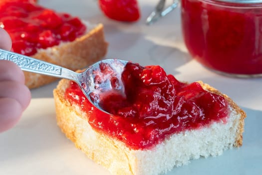 Spreading strawberry jam on a piece of wheat bread.