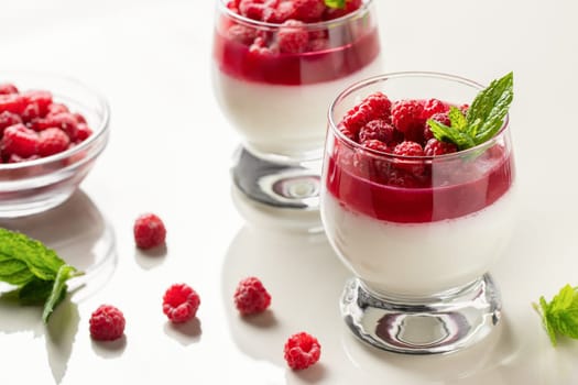 Panna cotta with raspberry jelly and mint leaves in glass glasses on a white table.