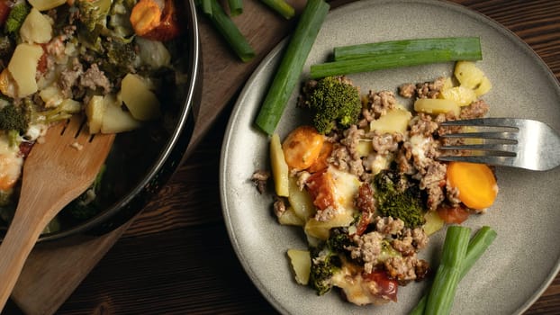 Portion of gratin with broccoli, carrots and cheese on a plate on a wooden table.