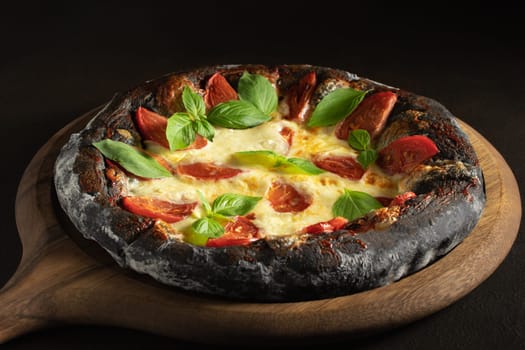 Black pizza margarita with tomatoes, mozzarella and basil. Dough with healthy bamboo charcoal powder.