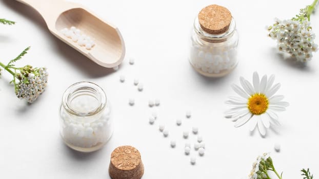 Composition of homeopathic medicines and medicinal plants on a white table.