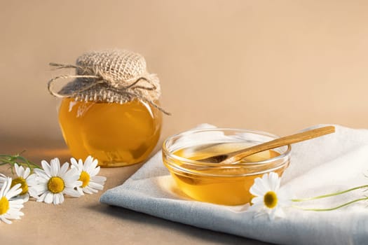 Chamomile syrup in a small bowl and in a jar and chamomile flowers on a linen kitchen towel, copy space.