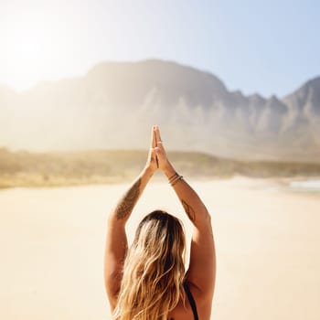 Live at peace with the world. Rearview shot of a young woman practising yoga on the beach