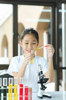 Schoolgirl is dropping a the liquid substance into the test tube with a long glass pipette in the scientific chemical laboratory. Education and Science concept.