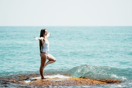 Woman sea yoga. Back view of free calm happy satisfied woman with long hair standing on top rock with yoga position against of sky by the sea. Healthy lifestyle outdoors in nature, fitness concept.