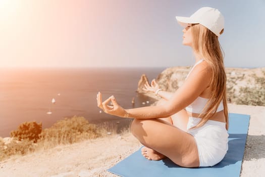 Woman meditating in yoga pose silhouette at the ocean, beach and rock mountains. Motivation and inspirational fit and exercising. Healthy lifestyle outdoors in nature, fitness concept.