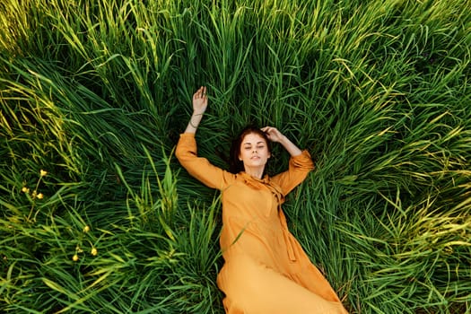 a joyful woman in a long orange dress lies in the tall green grass and looking at the camera smiles broadly. High quality photo