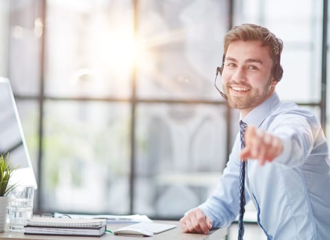 Young handsome male customer support phone operator with headset working in his office