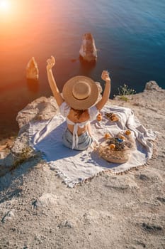 woman sea travel. photo of a beautiful woman with long blond hair in a pink shirt and denim shorts and a hat having a picnic on a hill overlooking the sea.