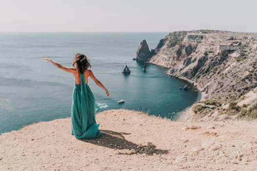 Woman green dress sea. Female dancer posing on a rocky outcrop high above the sea. Girl on the nature on blue sky background. Fashion photo