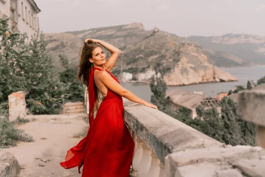 Woman red dress. Summer lifestyle of a happy woman posing near a fence with balusters over the sea