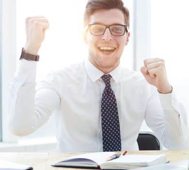 Happy young businessman raising hands in front of laptop