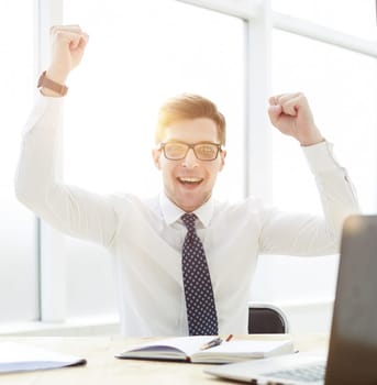 Happy young businessman raising hands in front of laptop