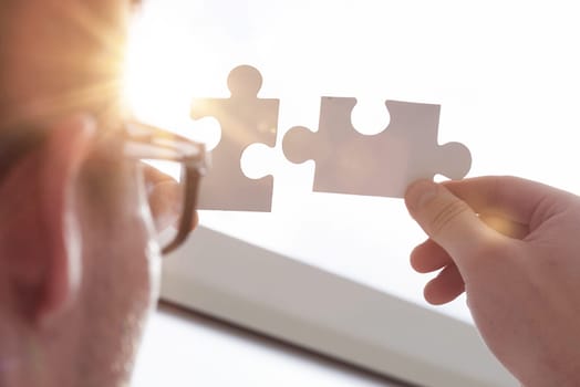 two hands of businessman to connect couple puzzle piece with sky background.Jigsaw alone wooden puzzle against sun rays