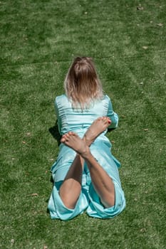 Woman grass park. Happy woman with blond curly hair in glasses and in a blue overalls lies on the summer fresh green grass with a phone in her hands